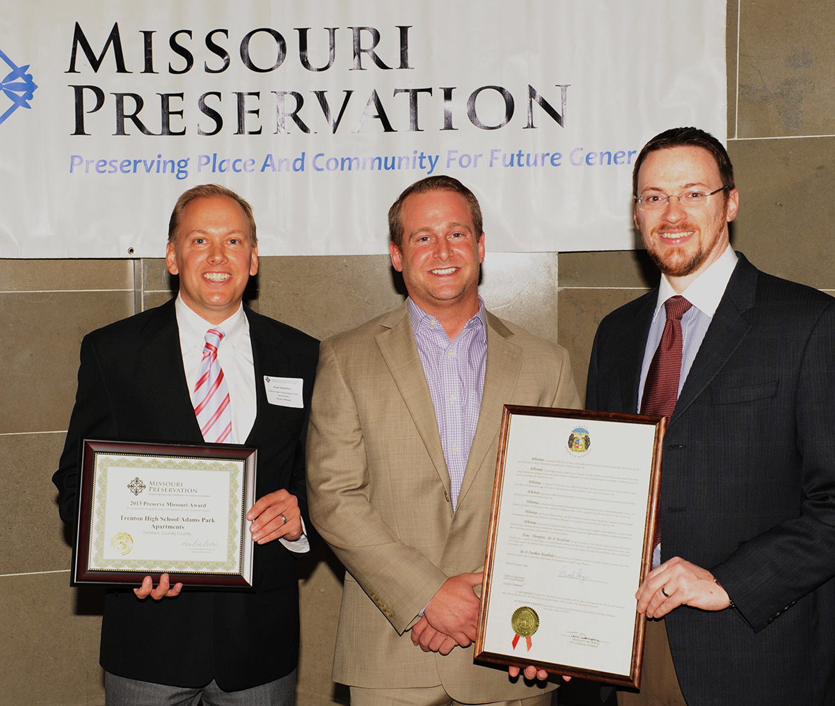 Ryan Hamilton, Vice President and Douglas Hamilton, construction supervisor, along with Mr. Rich Germinder fo the office of Missouri State Senator Brad Lager; display both the 2013 Preserve Missouri Award honoring Hamilton Properties Corporation for their successful conversion and preservation in the Adams Park School project, and a resolution from the Missouri State Senate honoring the Adams Park School project and receipt of the Preserve Missouri Award.